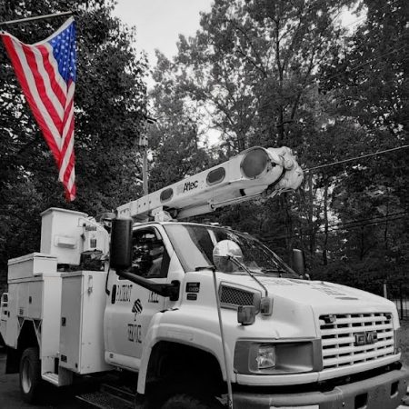 Striking black and white photo of a Patriot Tree Experts bucket truck with a full-color American flag attached to the boom, a branded tree service vehicle for Charleston, WV